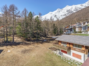 Un chalet doté d’un balcon, entouré d’une forêt et avec des montagnes enneigées en toile de fond.