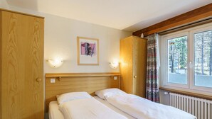Ein Zimmer mit einem Bett, einem Kleiderschrank, einem gerahmten Bild an der Wand und einem Fenster mit Vorhängen.
