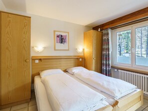 A room with two single beds, a wooden wardrobe, a framed picture on the wall, and a window with curtains. - Haus Alfa Appartement/Fewo 809, Einzimmer Whg Studio by Interhome (Saas-Fee)
