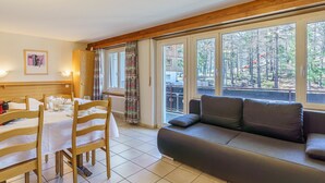 Ein Zimmer mit Esstisch für vier Personen, einer Couch und großen Fenstern mit Blick auf ein bewaldetes Gebiet.