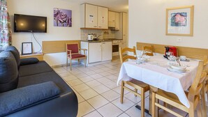 Ein modernes Wohnzimmer mit Flachbildfernseher, einer Couch und einem Essbereich mit Tisch für zwei Personen.