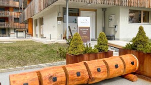 En hotelindgang med reception, loungeområde og butik. Træplanter med grønne planter og en unik træskulptur.