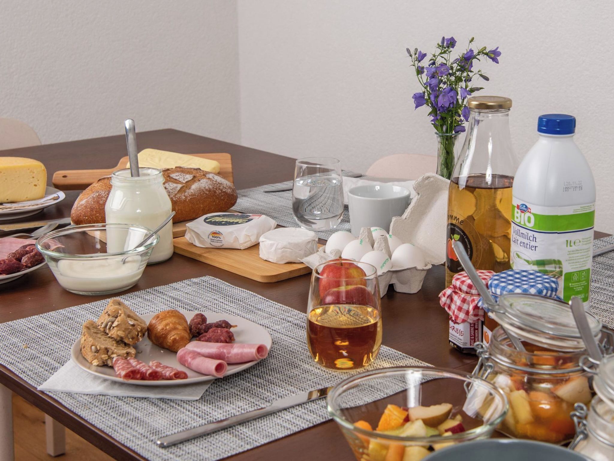 Desayuno con pan, queso, huevos y bebidas sobre una mesa.