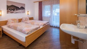 Una camera da letto con un letto di legno, un comodino, un'ampia finestra con tende e un bagno con lavandino e specchio.