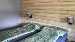 Huoneessa on kaksi sänkyä, puupaneloidut seinät ja kaksi seinälle asennettua lamppua.