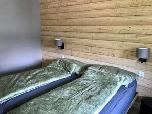 A room with two beds, wooden panel walls, and two wall-mounted lamps. - Amici 17 Appartement/Fewo 6-Bettwohnung by Interhome (Saas-Fee)