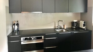 Moderni keittiö, jossa on mustat kaapit, ruostumattomasta teräksestä valmistettu liesi, sisäänrakennettu uuni, pesuallas ja kahvinkeitin.