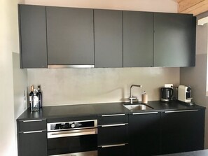 A modern kitchen with black cabinets, a stainless steel range, a built-in oven, a sink, and a coffee maker. - Amici 17 Appartement/Fewo 6-Bettwohnung by Interhome (Saas-Fee)