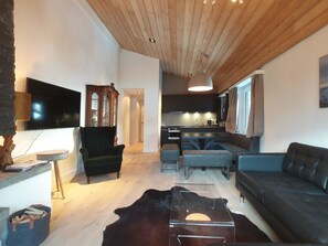 A modern living room with a flat-screen TV, a dark green armchair, a black leather sofa, and a wooden ceiling. - Amici 17 Appartement/Fewo 6-Bettwohnung by Interhome (Saas-Fee)