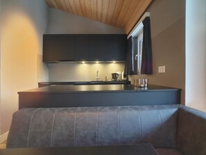 A modern kitchen with dark cabinetry, a built-in island, and a seating area with a cushioned bench. - Amici 17 Appartement/Fewo 6-Bettwohnung by Interhome (Saas-Fee)