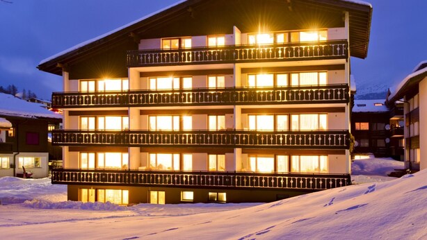 A multi-story hotel with balconies, snow-covered surroundings, and illuminated windows. - Haus Alfa Appartement/Fewo 806, Einzimmer Whg Studio by Interhome (Saas-Fee)