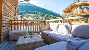 Eine Holzterrasse mit Korbmöbeln und Blick auf ein dörfliches Bergdorf.