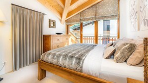 Ein Schlafzimmer mit einem hölzernen Bett, einem Schminktisch, einem Fenster mit Vorhängen und Blick auf einen Balkon.