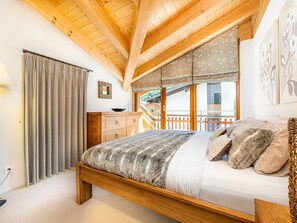 A bedroom with a wooden bed, a dresser, a window with curtains, and a view of a balcony. - Sonnegg Penthouse Appartement/Fewo 10-Bettwohnung by Interhome (Saas-Fee)