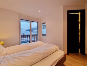 Ein Schlafzimmer mit einem Bett, einem Fenster mit Bergblick und einer Tür zu einem anderen Raum.