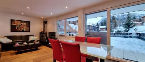 Un salon moderne avec une table à manger en verre et des chaises rouges, un canapé noir et un tableau accroché au mur.