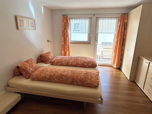 Ein Schlafzimmer mit zwei Betten, einem Kleiderschrank und einem Balkon mit Vorhängen.