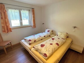 A room with two single beds, a window with curtains, a wooden floor, and a small chair. - Alpenstern Appartement/Fewo 6-Bettwohnung "Trift" by Interhome (Saas-Grund)