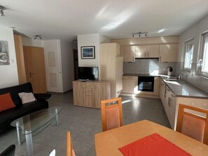 Ein kompakter Wohnbereich mit Küchenzeile, Essplatz und Wohnzimmer mit Sofa und Fernseher.
