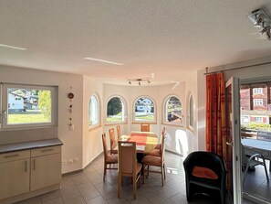 Ein Essbereich mit Tisch und Stühlen, eine Küchenzeile mit Schränken und große Fenster mit Rundbögen.
