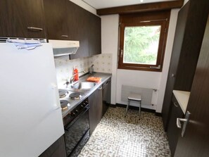 Een compacte keuken met donkerhouten kastjes, een witte koelkast, een gasfornuis en een raam dat voor natuurlijk licht zorgt.