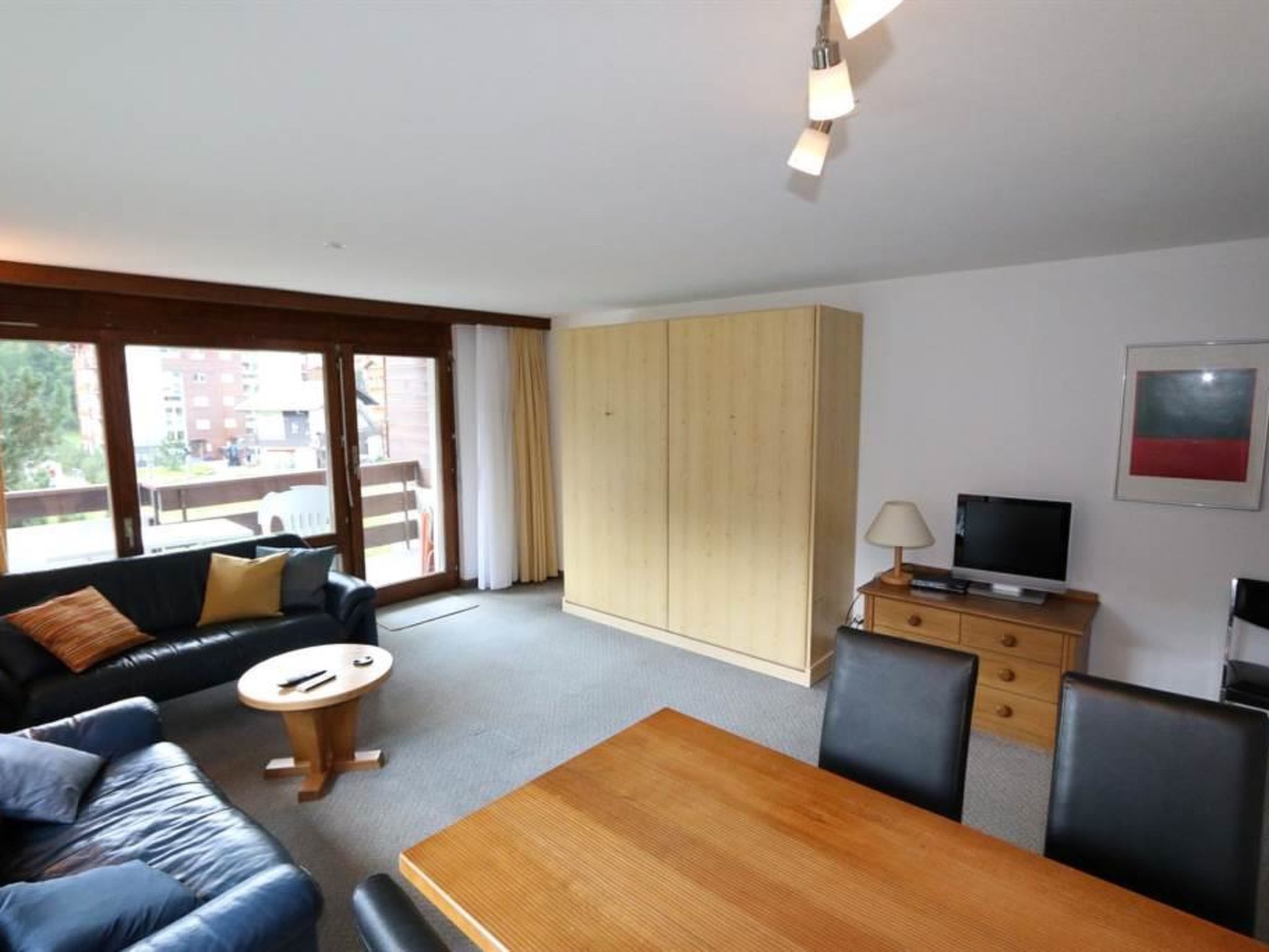 Habitación de hotel con sofá, una mesa de madera, televisión, armario y ventana con vistas a edificios.