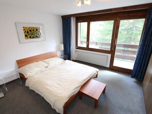 Een slaapkamer met een bed, een bankje, een raam en een radiator.