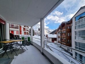 A balcony with a table and chairs, a railing, and a view of snow-covered mountains and buildings. - Daniela 2 Appartement/Fewo Appartement/Fewo by Interhome (Saas-Fee)