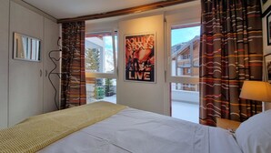 Une chambre à coucher avec un lit, une fenêtre avec des rideaux, une affiche accrochée au mur et une porte donnant sur l’extérieur.