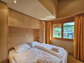Une chambre d’hôtel avec un lit, une tête de lit en bois, une fenêtre avec des rideaux et une vue sur une région montagneuse.