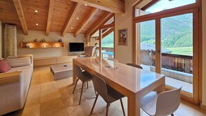 Un amplio salón con techo de madera, una mesa de comedor con sillas, un sofá y un televisor.