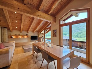 A spacious living area with a wooden ceiling, a dining table with chairs, a sofa, and a television. - Aramis 4. OG Appartement/Fewo Aramis 4. OG | 6-Bettwohnung by Interhome (Saas-Fee)