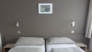 A hotel room with two single beds, a nightstand on each side, a wall-mounted light, and a painting above the beds. - Mischi 9 & 10 Appartement/Fewo 5-Bettwohnung Nr. 9 by Interhome (Saas-Fee)