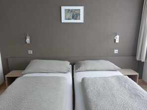 Habitación de hotel con dos camas individuales, una mesita de noche a cada lado, una lámpara de pared y un cuadro sobre las camas.