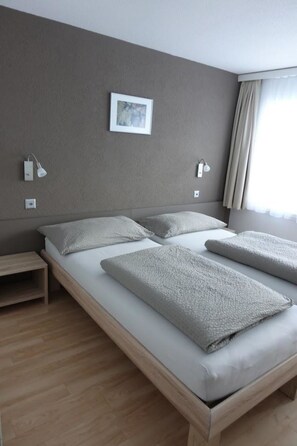 A hotel room with a large bed, bedside lamps, a small table, and a window with curtains. - Mischi 9 & 10 Appartement/Fewo 5-Bettwohnung Nr. 9 by Interhome (Saas-Fee)