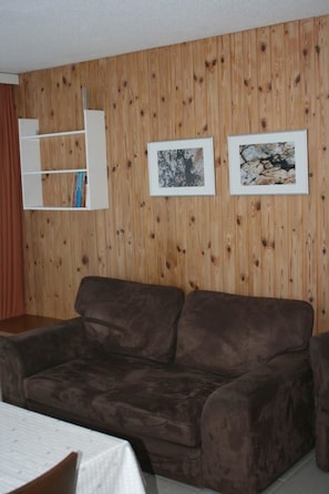 A room with a brown sofa, a white shelf with books, and two framed pictures on the wall. - Mischi 9 & 10 Appartement/Fewo 5-Bettwohnung Nr. 9 by Interhome (Saas-Fee)