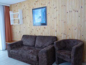 Una habitación con un panel de madera, un sofá marrón, una silla y un cuadro enmarcado.