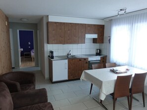 Cocina compacta con muebles de madera, un lavamanos y un comedor con mesa y sillas.