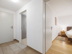 Un dormitori modern amb un terra de fusta, un llit amb capçalera, una taula de nit amb una làmpada i una porta que dona a una altra habitació.