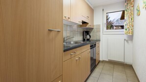 Eine Küche mit Holzschränken, einer Arbeitsplatte, einer Kaffeemaschine und einem Fenster mit Vorhängen.