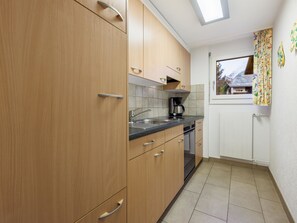 A kitchen with wooden cabinets, a countertop, a coffee maker, and a window with curtains. - Everest Appartement/Fewo 4-Bettwohnung K by Interhome (Saas-Fee)
