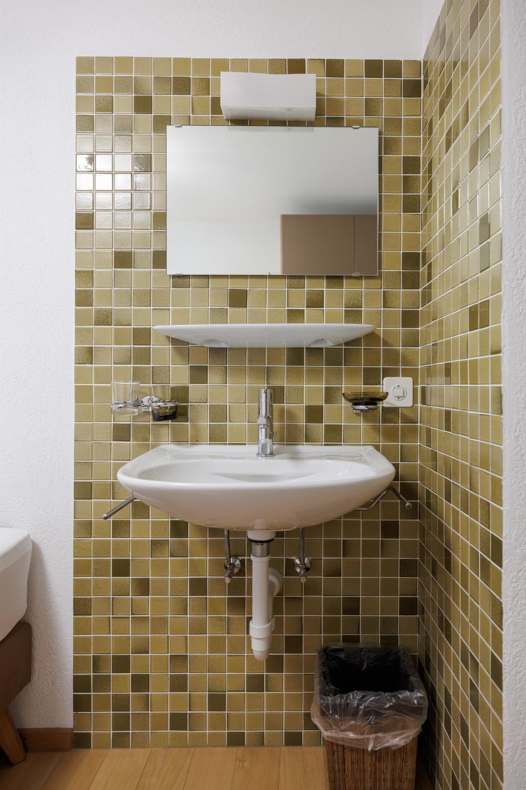 Un baño con lavamanos blanco, espejo y salpicadero de azulejos.