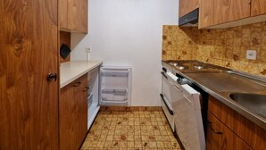 Eine kompakte Küche mit Holzausstattung, einem eingebauten Backofen und einer Edelstahlspüle.