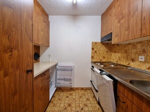 Eine kompakte Küche mit Holzausstattung, einem eingebauten Backofen und einer Edelstahlspüle.