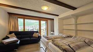 Ein Zimmer mit einer schwarzen Couch, einem Bett mit gemusterten Betttextilien, einem Fenster mit Vorhängen und Blick auf eine Stadt.