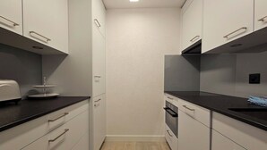 Eine schmale Küche mit weißen Schränken, schwarzen Arbeitsplatten und Holzboden.