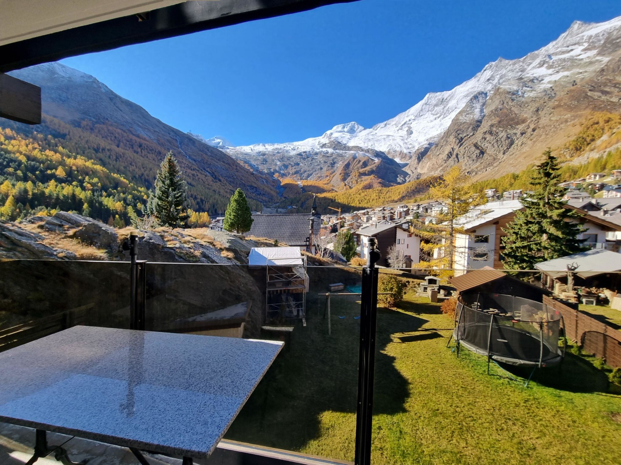A mountain village with traditional houses, a clear sky, and snow-capped peaks in the background.