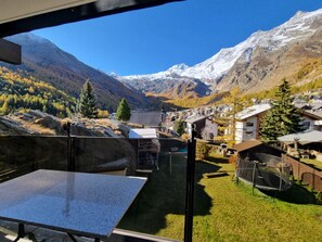 Ein Bergdorf mit traditionellen Häusern, wolkenlosem Himmel und schneebedeckten Gipfeln im Hintergrund.