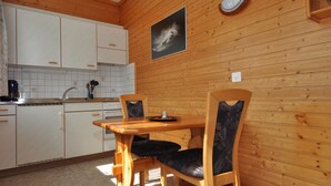Cocina con paneles de madera, armarios blancos, una mesa de comedor con sillas y una lámpara fijada a la pared.