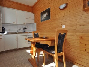 A wooden-paneled kitchen with white cabinets, a dining table with chairs, and a wall-mounted light fixture. - Chalet Ideal Appartement/Fewo 2-Bettwohnung Nr. 1 by Interhome (Saas-Fee)
